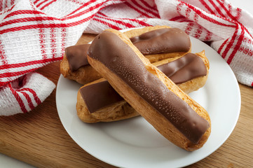 French cuisine and baked desserts concept with whip cream and chocolate eclairs on a plate in a rustic kitchen with a tea towel in the background