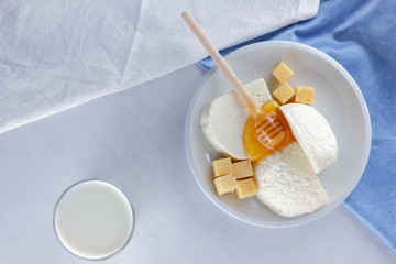 Cheese, milk assortment on white background, white cheese and honey on a blue napkin, wooden background, wooden stick for honey, top view, cheese on white plate, kefir in a glass