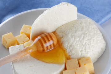 Cheese, milk assortment on white background, white cheese and honey on a blue napkin, wooden background, wooden stick for honey, top view, cheese on white plate, kefir in a glass