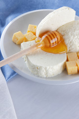 Cheese, milk assortment on white background, white cheese and honey on a blue napkin, wooden background, wooden stick for honey, top view, cheese on white plate, kefir in a glass