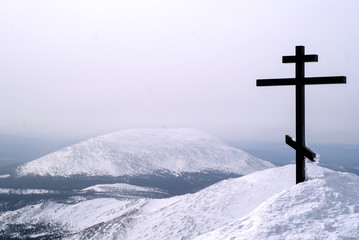 Fototapeta na wymiar orthodox cross on top of the mount Konzhakovskiy Kamen against the background of the surrounding winter mountains