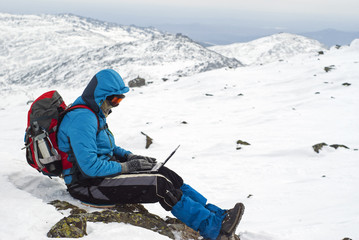 traveler working with a laptop in winter on top of a mountain during the snowfall - obrazy, fototapety, plakaty