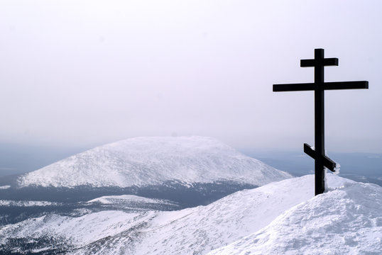 orthodox cross on top of the mount Konzhakovskiy Kamen against the background of the surrounding winter mountains