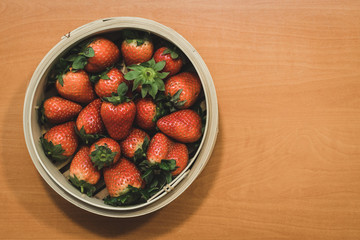 A basket full of beautiful strawberries on top of a wooden table. They are at the perfect point of maturation.