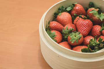 A basket full of beautiful strawberries on top of a wooden table. They are at the perfect point of maturation.