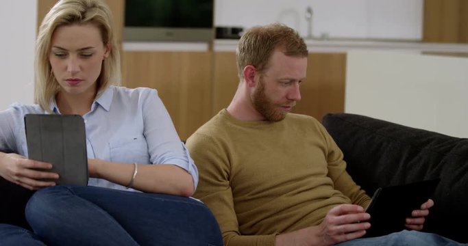 Attractive couple surf on tablets whist ignoring each other, showing what is wrong with modern technology, in slow motion
