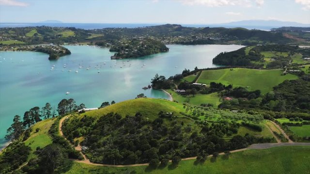 Drone shot green hills and blue ocean with yachts in bay.