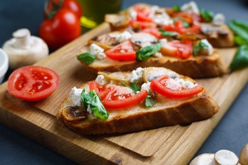 Tasty crunchy italian snack bruschetta with chopped tomatoes and champignons, garnished with ricotta and basil on wooden board
