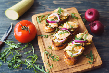 Tasty crunchy italian snack bruschetta with grilled zucchini and chicken, garnished with arugula and pink onion on wooden board