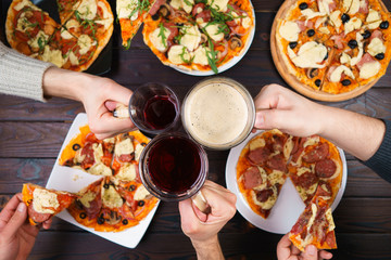 Friends eating pizza. Top view on male hands clinking mugs with beer over table with many pizzas. Party, friendship, pub, restaurant concept