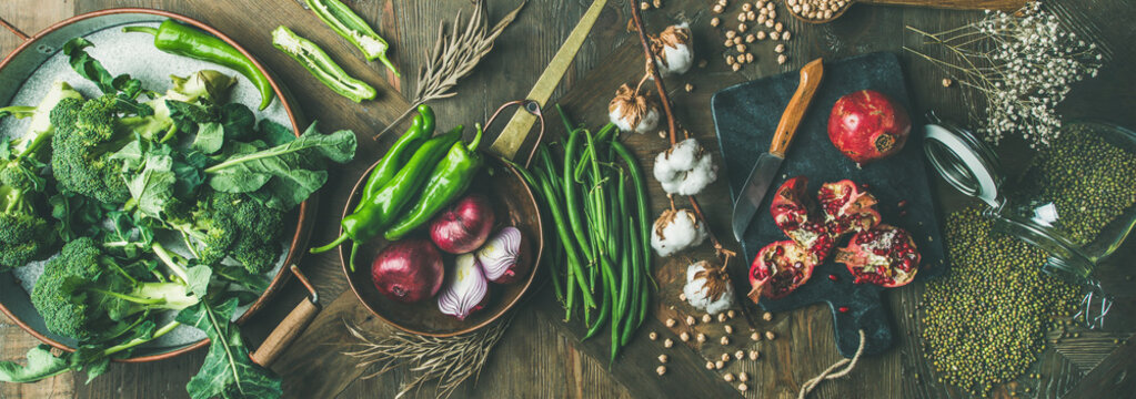 Winter vegetarian, vegan food cooking ingredients. Flat-lay of seasonal vegetables, fruit, beans, cereals, kitchen utencils, dried flowers, olive oil over wooden background, top view, wide composition
