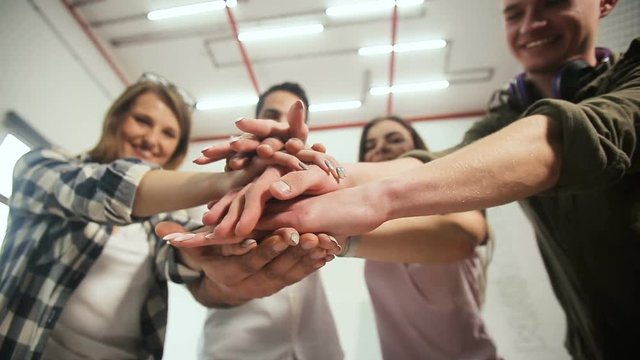 Young and motivated team of workers doing togetherness gesture, standing happily in the middle of modern white office