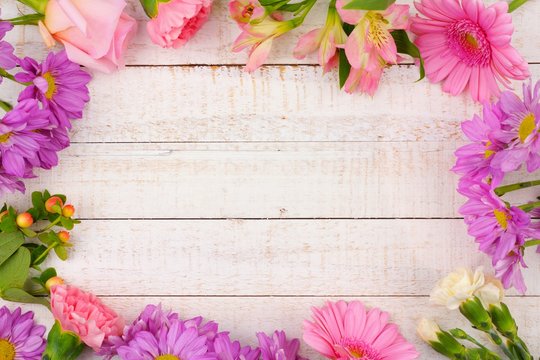 Frame of pink and purple flowers with rose, carnations, lilies and daisies against a white wood background. Copy space.