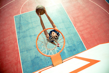 Young man jumping and making a fantastic slam dunk playing streetball, basketball. Urban authentic.