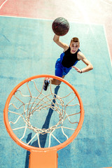 Young man jumping and making a fantastic slam dunk playing streetball, basketball. Urban authentic.
