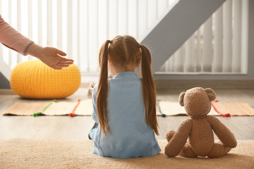 Female psychologist offering her hand to sad little girl indoors