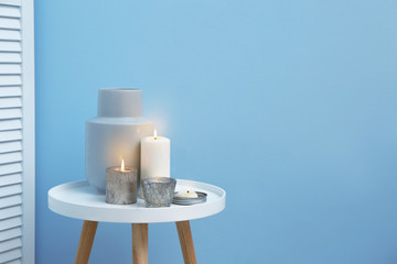 Beautiful burning candles on table near color wall