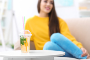 Cup with tasty refreshing lemonade and blurred woman on background