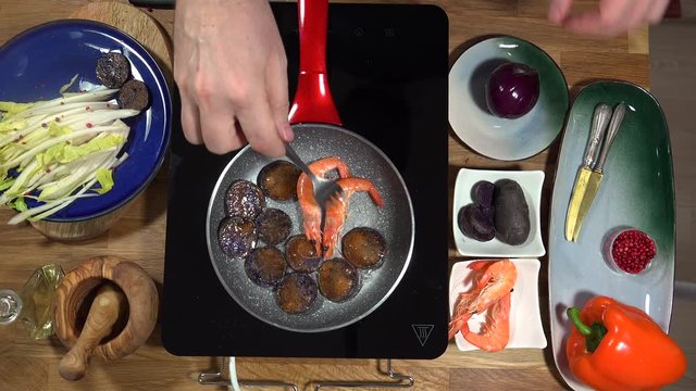 Top view food preparation Shrimp and violet potatoes to the pan on the stove with induction
