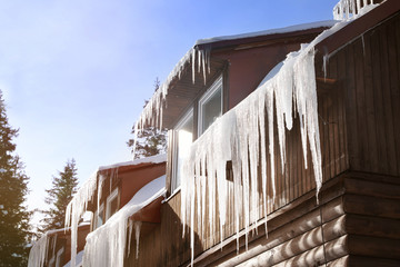 Wooden house with icicles on winter day - obrazy, fototapety, plakaty