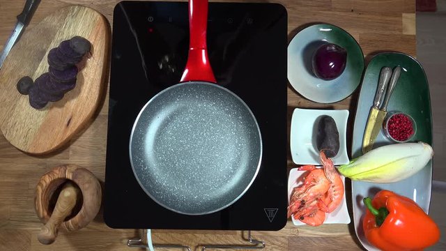 Top view food preparation Shrimp and violet potatoes to the pan on the stove with induction