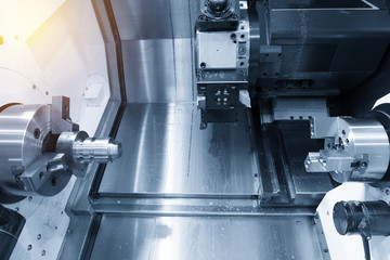 The  CNC lathe machine cutting the steel rod in the light blue scene.The  modern machining process.