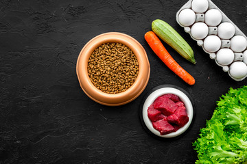 Dry pet food with natural ingredients. Raw meat, cut vegetables zucchini and carrot, eggs on black backgroud top view mock-up