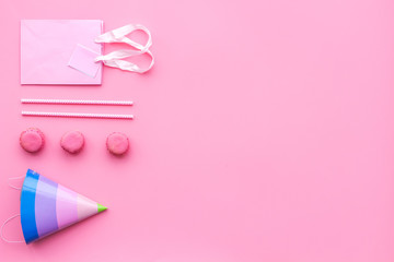 Birthday party accessories. Party hat, sweets, paper bag for gift on pink background top view copy space pattern
