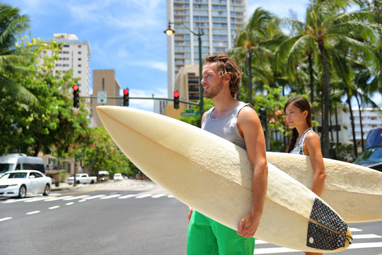 Honolulu Hawaii lifestyle surfers people walking in city with surfboards going to the beach surfing. Outside hawaiian surf living. Surfer couple crossing street. Waikiki, Honolulu, Oahu, Hawaii, USA.