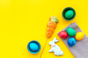 Colorful easter eggs with sweets gingerbread on yellow background top view mockup