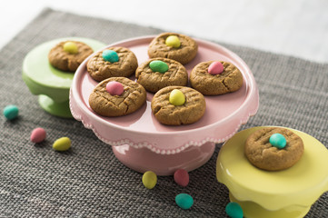 Easter eggs cookies baked sweets. Homemade peanut butter cookies desserts with a Easter holiday twist! Chocolate mini easter eggs are added on top of each cookie. Served on colorful pastel cake stands