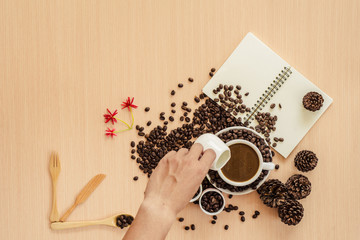 Man mixingwhite milk into cup of coffee with coffee beans background, copy space