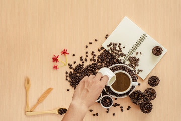 Man mixingwhite milk into cup of coffee with coffee beans background, copy space