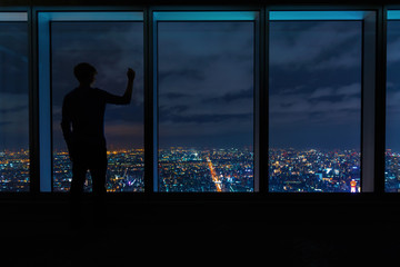 Fototapeta na wymiar Man writing on large windows high above a sprawling city at night