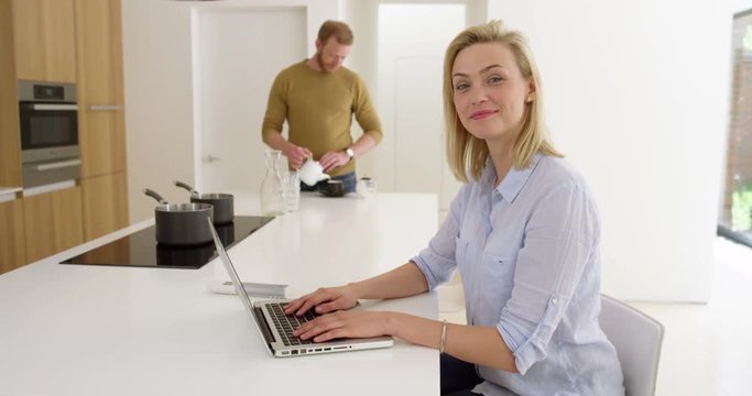 Portrait of attractive woman working from home on laptop and with husband in beautiful contemporary kitchen, in slow motion