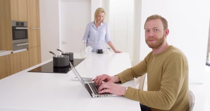 Portrait of handsome man works from home on laptop and with wife in beautiful contemporary kitchen, in slow motion