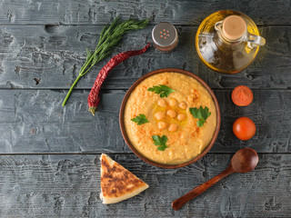 Fresh hummus, wooden spoon, a piece of lavash, tomatoes on a wooden table. The view from the top.