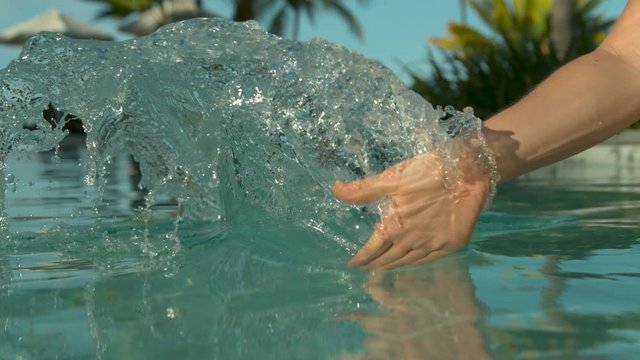 SLOW MOTION, CLOSE UP: Unrecognizable female tourist drags her hand through calm pool water and creates a ripple. Caucasian woman plays in the stunning pool of a exotic hotel resort in Fiji Islands.