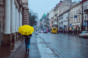 woman walk by side walk with yellow umbrella. rainy weather in old european city