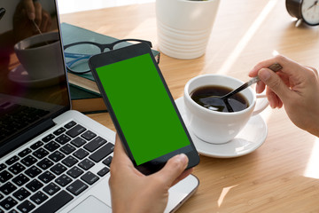 Top view of smartphone green screen display with hand, laptop, coffee cup and glasses.