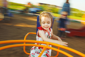 little girl spinning on a children's carousel among the playground.