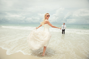 Fototapeta na wymiar bride in wedding dress runs to bridegroom over sea turning back. lucky woman on the beach.