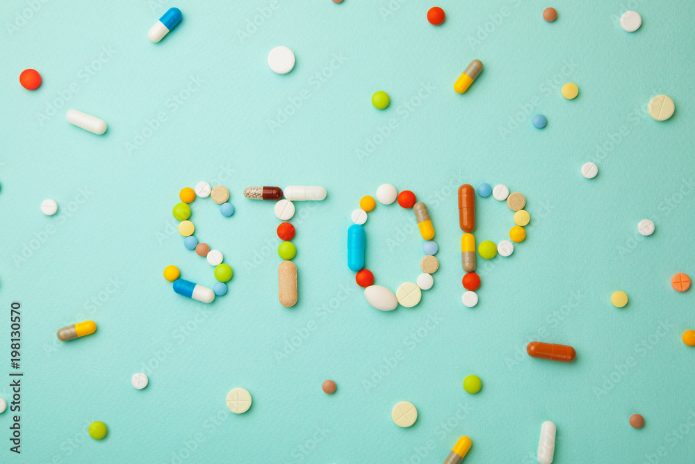 Wall mural word stop from colored pills and capsules on green background. medicines and tablets kill