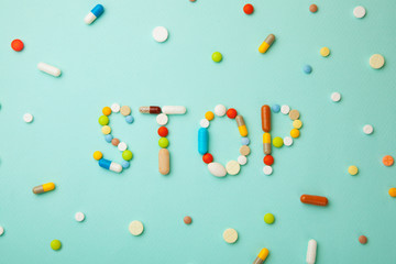 Word STOP from colored pills and capsules on  green background. Medicines and tablets kill