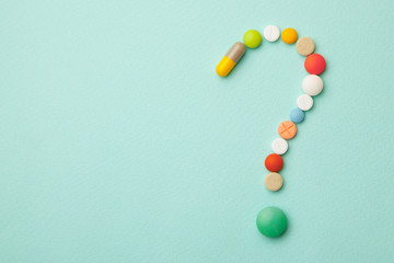 Symbol question mark from colored tablets and capsules on  green background. What medicines to...