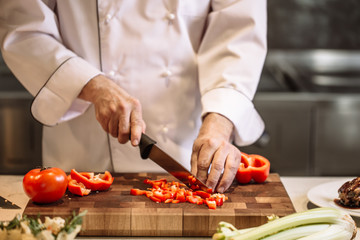 close-up cropped photo of man's hands chopping up red peppers indoor. hardworking chef