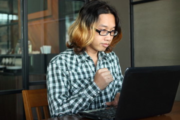 Successful and confident young Asian hipster with casual clothes working with laptop for his job in workplace of office.