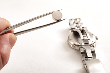 watchmaker is working to replace the battery on an old quartz metal watch in his repair shop, he is...