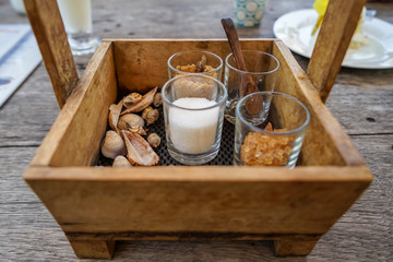 Vintage wooden box basket holding sugar glasses and spoon for coffee and tea with sea shell decoration on wooden table, selective focus