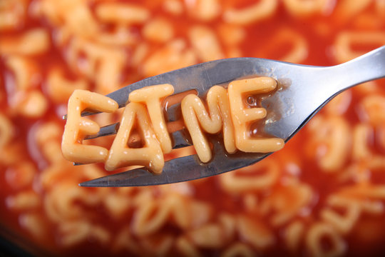 Spaghetti letter spelling the word 'Eat Me' with the letters held up on a fork.